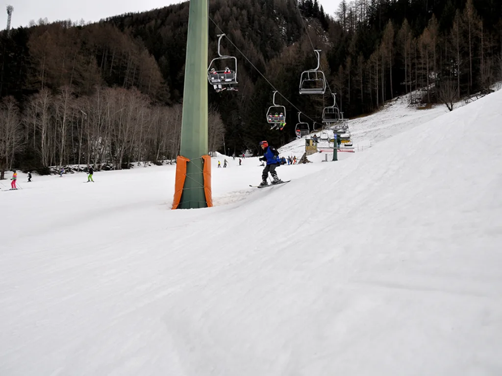 Skifahrer in blauer Jacke auf dem Hang neben dem Lift.